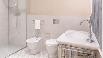 A bathroom with a glass-enclosed shower, a bidet, a toilet, and a sink with a mirror.