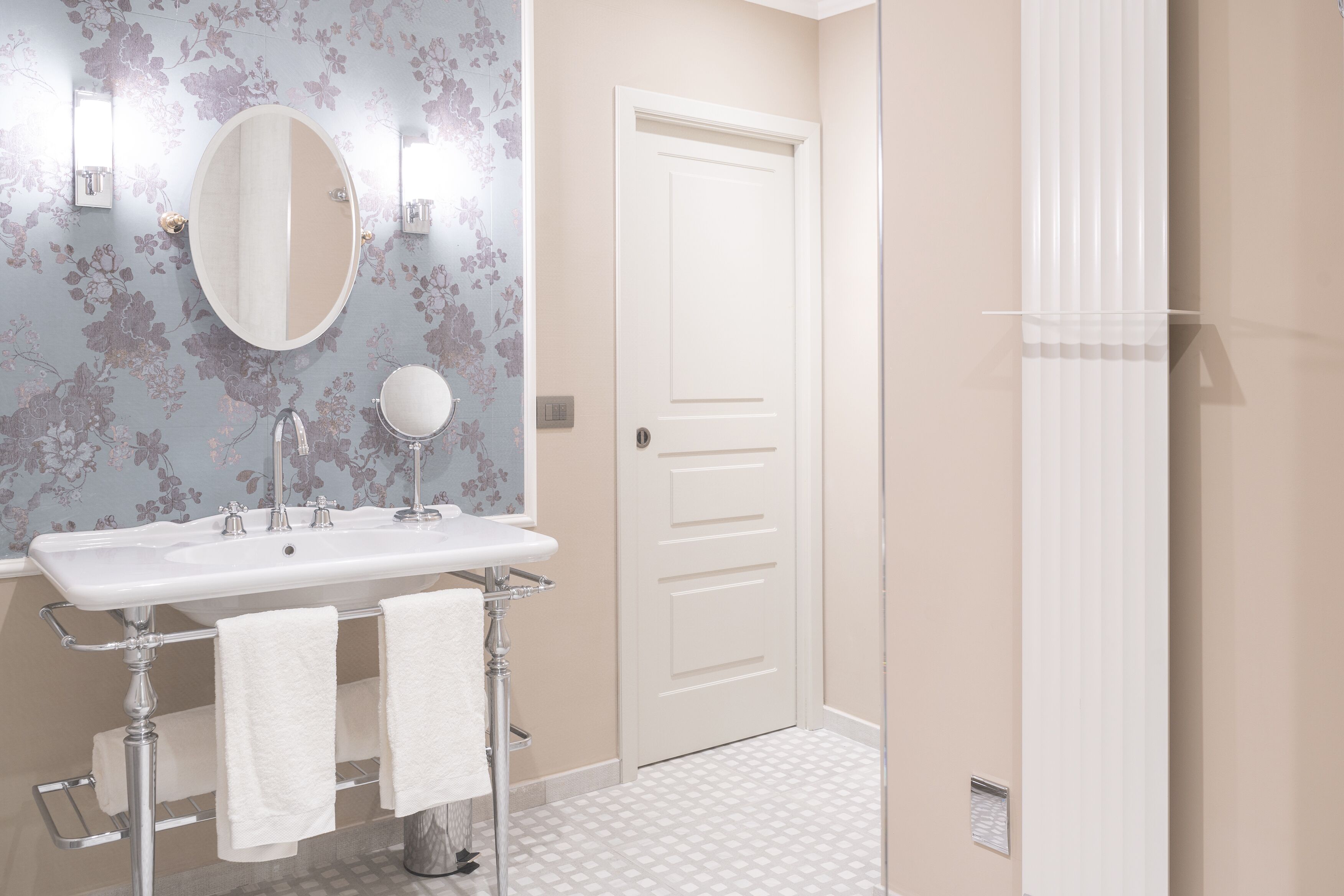 A bathroom with a white sink, two mirrors, a towel rack, and a door.