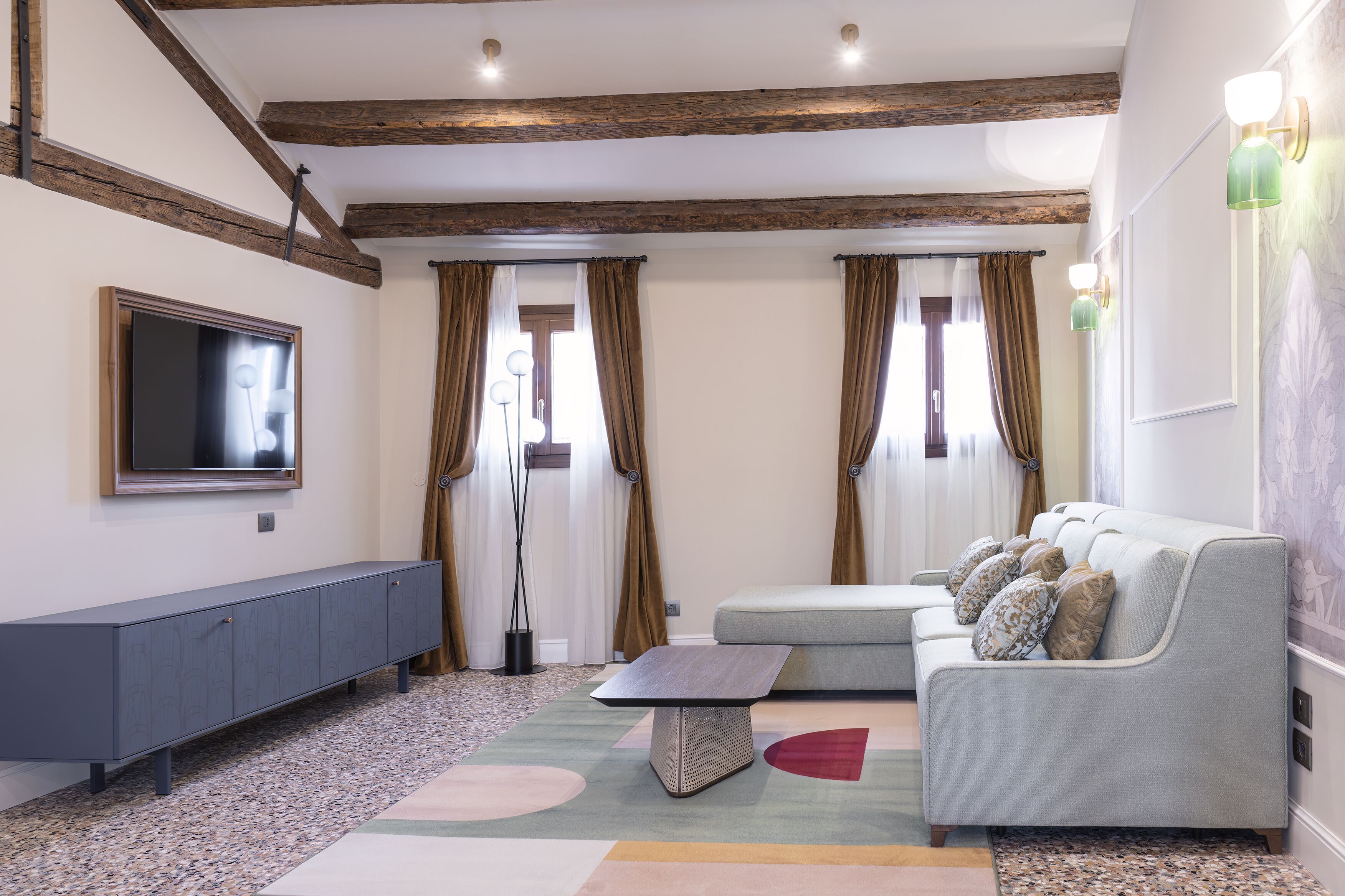 A modern living room with a grey sofa, a flat-screen TV, and a patterned rug.