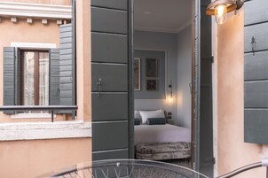 A room with a bed, a window with shutters, and a wall-mounted light fixture.