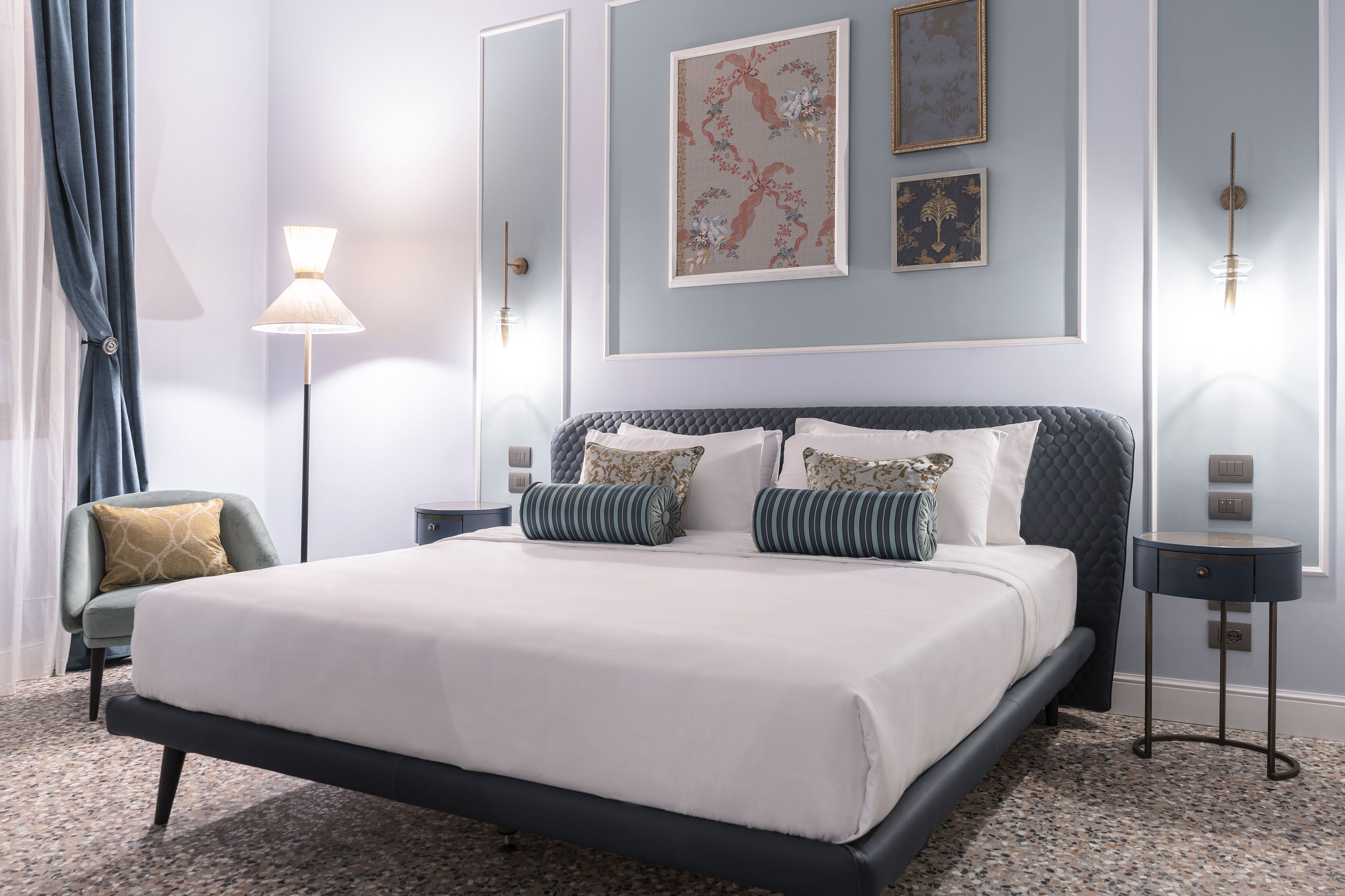 Un dormitorio con cama, una silla, una lámpara y decoración en la pared.