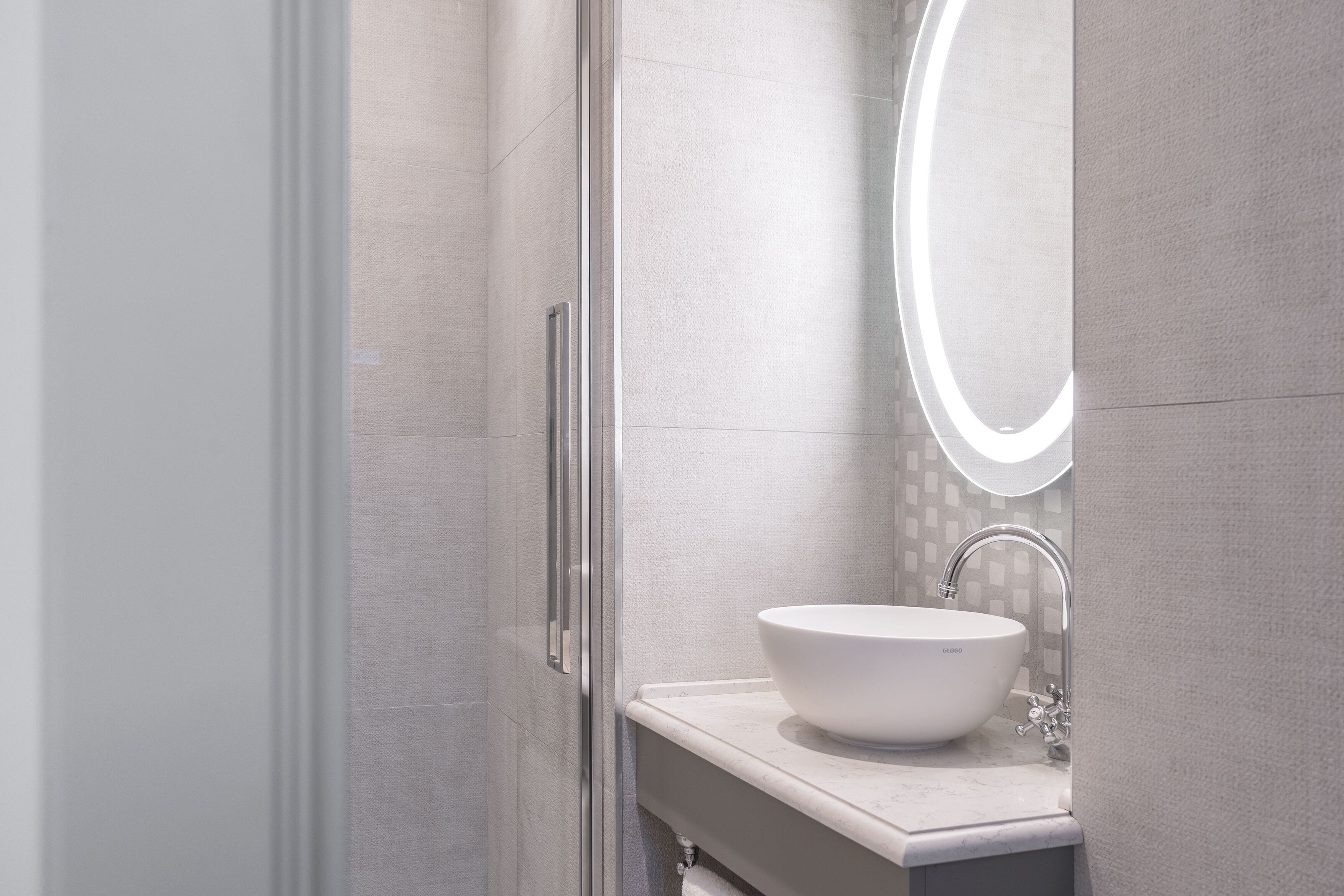 Een moderne badkamer met een wit wastafelmeubel, een spiegel met verlichting en een douchehoek.