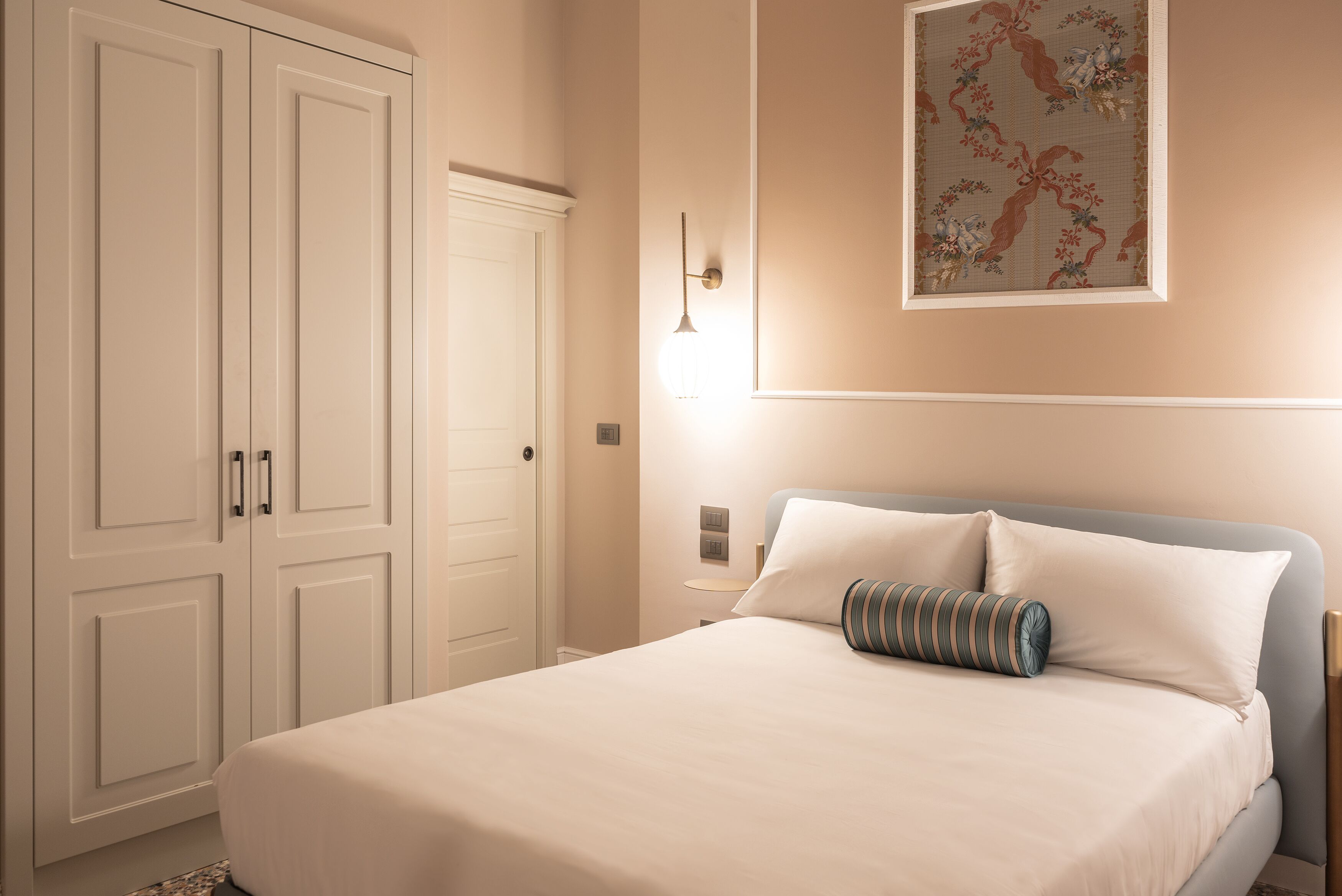 A bedroom with a bed, a nightstand, a wall-mounted lamp, and a wardrobe.