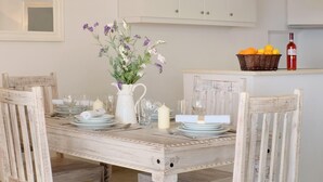 A rustic dining table set with white plates, glasses, and a vase of flowers. - The Saints - St Mathias 2 Bedroom Cottage (Corfu)