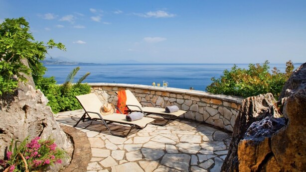 A stone patio with two lounge chairs and a table, overlooking a body of water. - The Saints - St Mathias 2 Bedroom Cottage (Corfu)