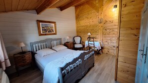 Ein Schlafzimmer einer Holzhütte mit einem Bett, Nachttischen, einem Sessel und einem kleinen Tisch mit einer Lampe.