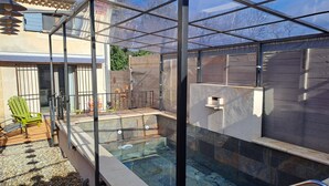 Ein von Glas umgebener Swimmingpool mit einer steinverkleideten Terrasse und einem Holzzaun.