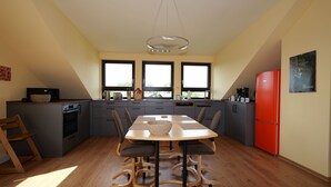 A modern kitchen with a central island, a dining table with chairs, and a red refrigerator. - Vacation apartment Stifterfelsen (Sinzing)
