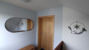 A hallway with a wooden door, a wall-mounted mirror, and a decorative wall piece with the word "Servus". - Vacation apartment Stifterfelsen (Sinzing)