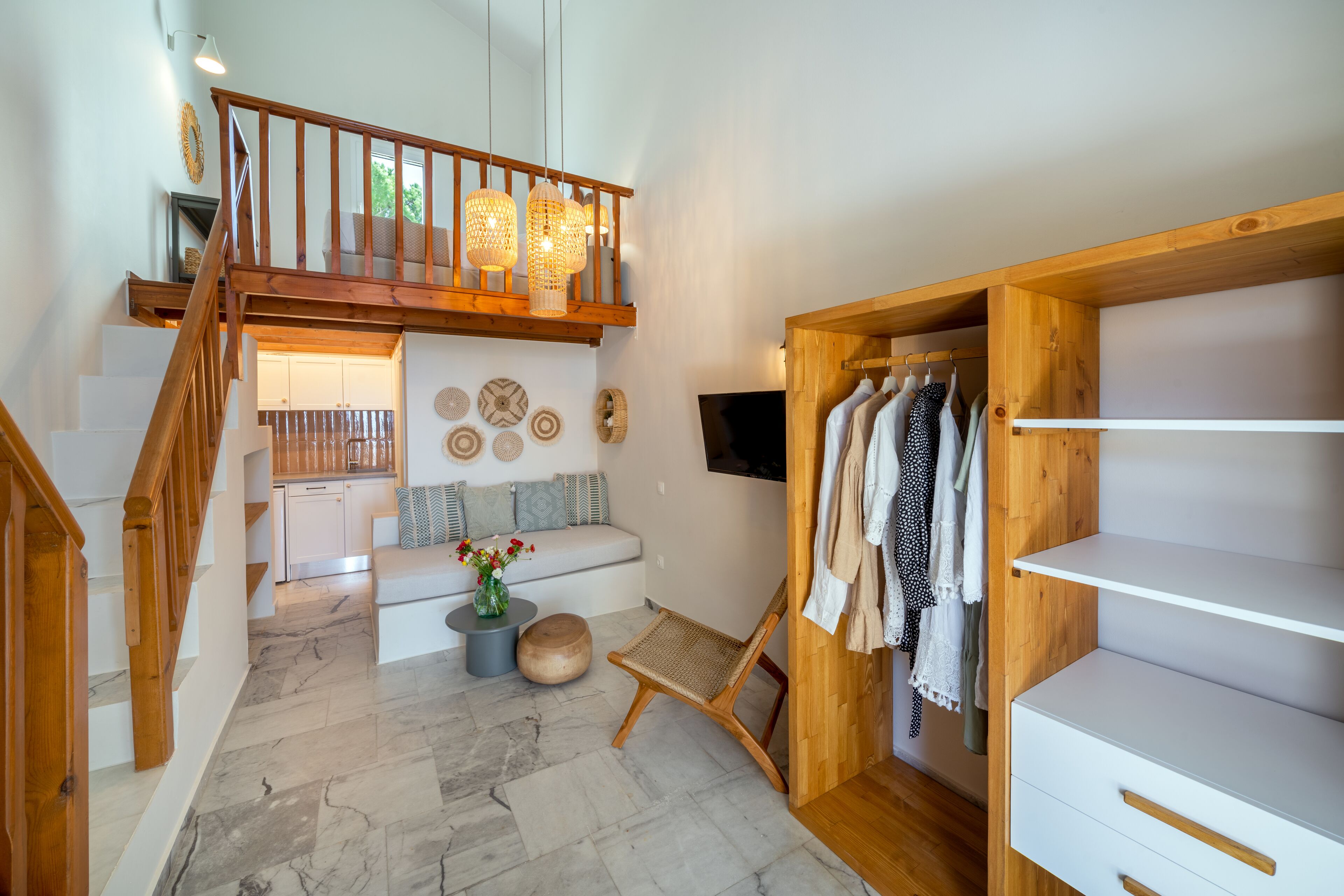 Un vaste espace de vie agrémenté d’un escalier en bois, d’un coin salon avec un canapé et des coussins, d’une petite table sur laquelle est posé un vase, et d’un banc en bois.