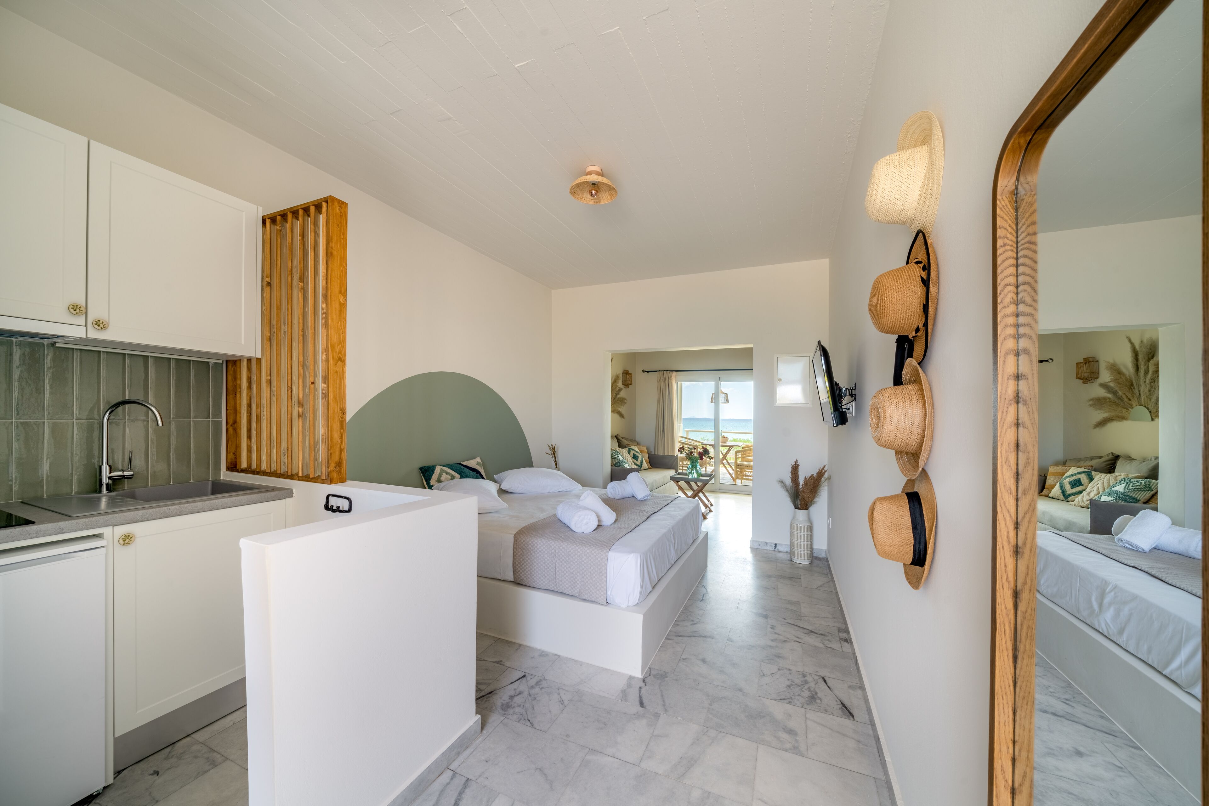 A modern bedroom with a large bed, a small kitchen area, and a bathroom visible through an open door.