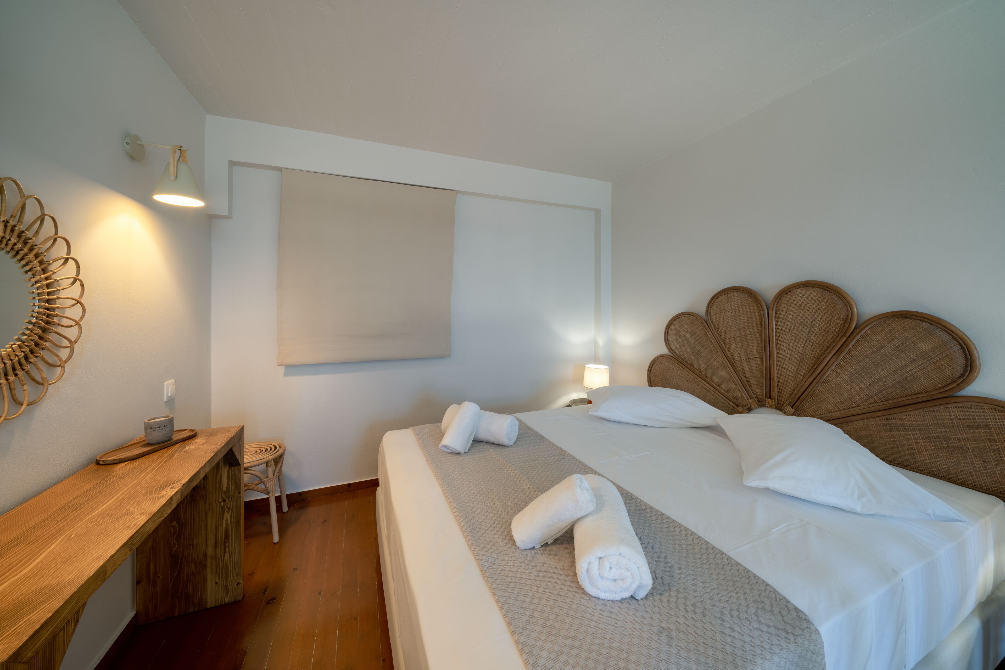 A neatly arranged hotel room with a bed, a wooden desk, a chair, and a wall-mounted mirror.