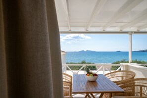 A covered outdoor seating area with a table and wicker chairs, overlooking a scenic ocean view. - Grand Bleu Anastazia (Ermionida)