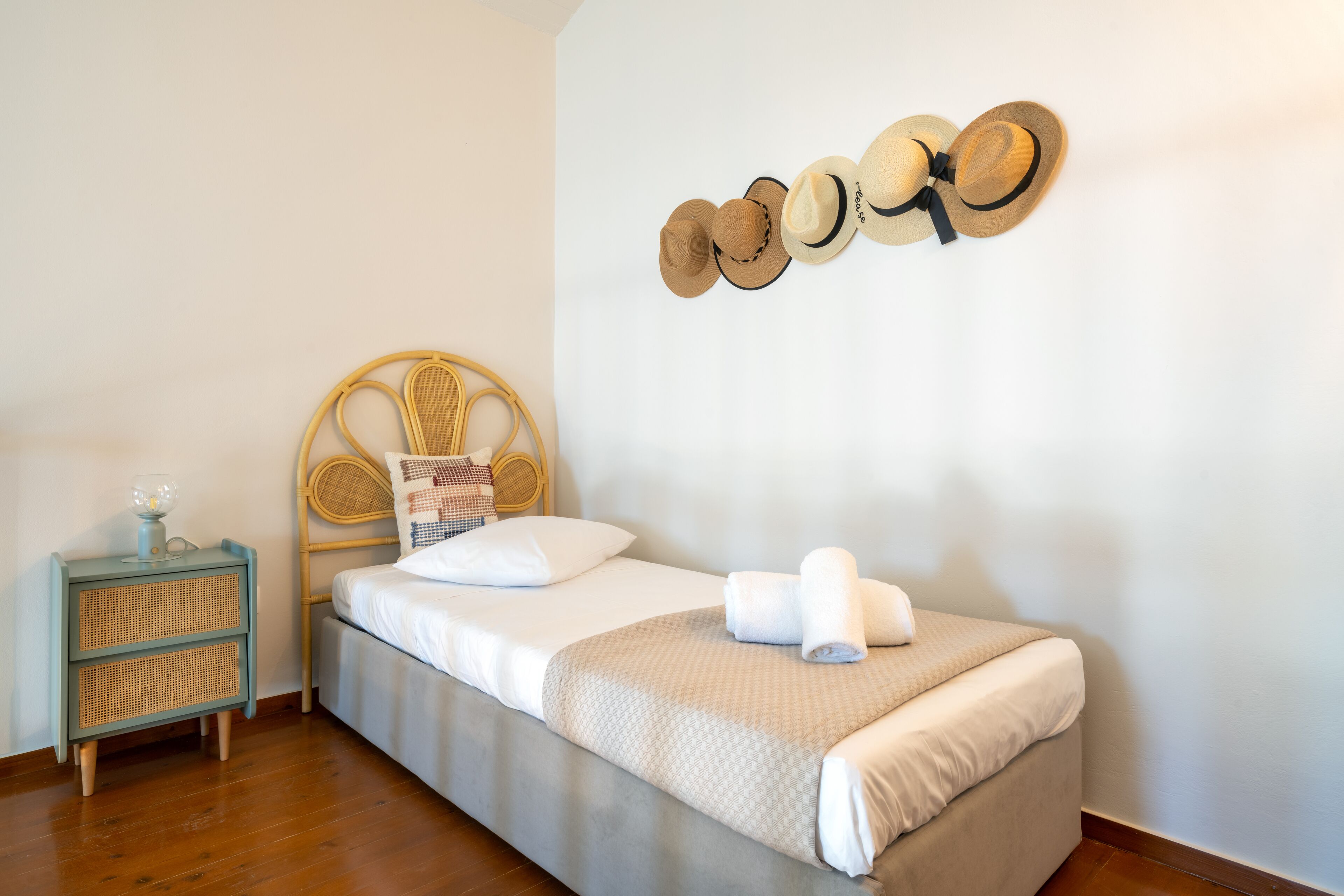 A neatly made bed with a headboard, a bedside table with a lamp, and a wall-mounted hat rack.