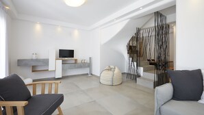 Una sala de estar moderna con un televisor de pantalla plana, dos sofás, un sillón de peluche y una escalera con un diseño único en blanco y negro.