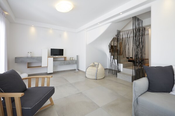 A modern living room with a flat-screen TV, two sofas, a bean bag, and a staircase with a unique black and white design.