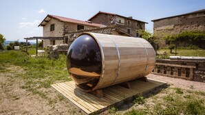 Uma grande estrutura em forma de barril de madeira com superfície reflexiva, localizada ao ar livre com um edifício de pedra ao fundo.
