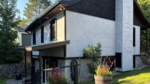 Una casa moderna de dos pisos con un porche cubierto, pared de piedra y plantas en macetas.