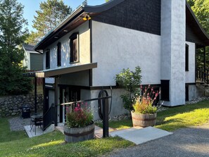 A modern two-story house with a covered patio, stone wall, and potted plants.