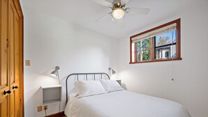 A bedroom with a bed, a window, a ceiling fan, and a wooden door.