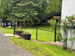 Un edificio moderno con terraza de madera, barandilla metálica y jardín con arbustos y flores.
