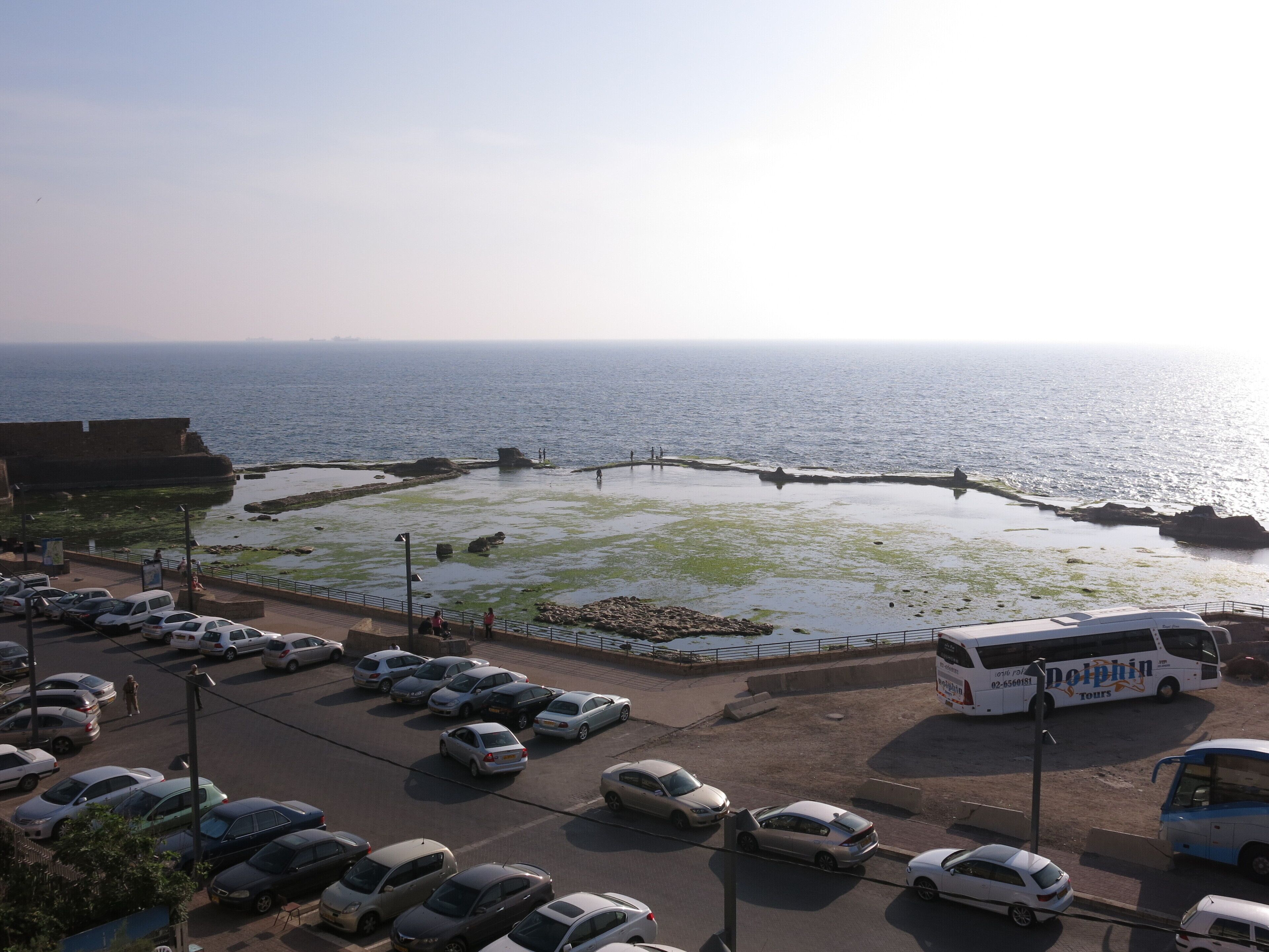 A coastal parking area with a bus and cars, overlooking the sea.