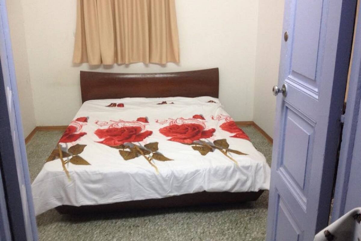 Un dormitorio pequeño con cama, cabecera de madera, cortina color beige y una puerta cerrada.