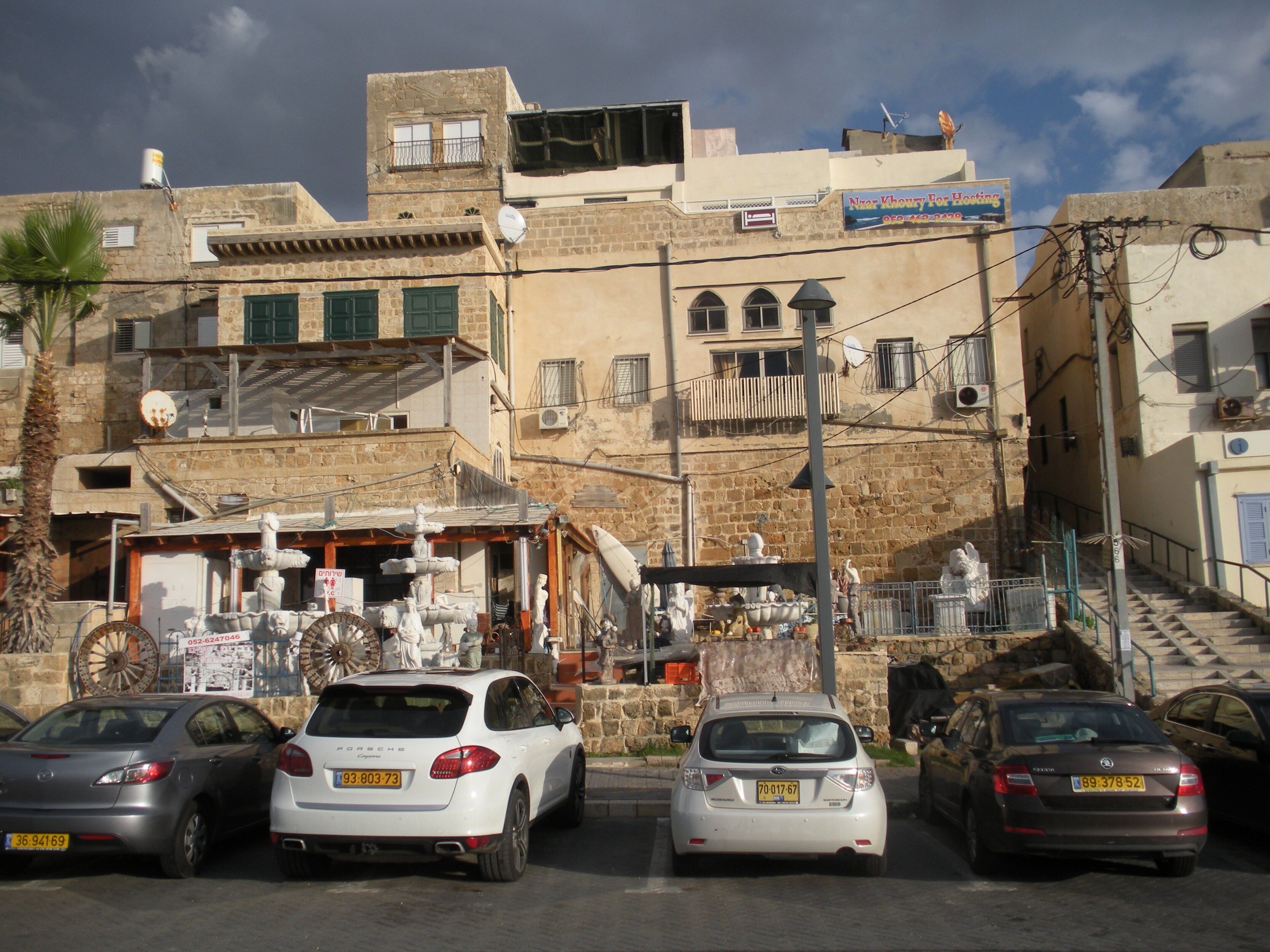 A street view with parked cars, a building with a sign for a roofing service, and a staircase leading to an upper level.