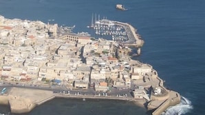 An aerial view of a coastal town with a fortified harbor, dense urban area, and a prominent church. - Nzar Khoury For Hosting (Acre)