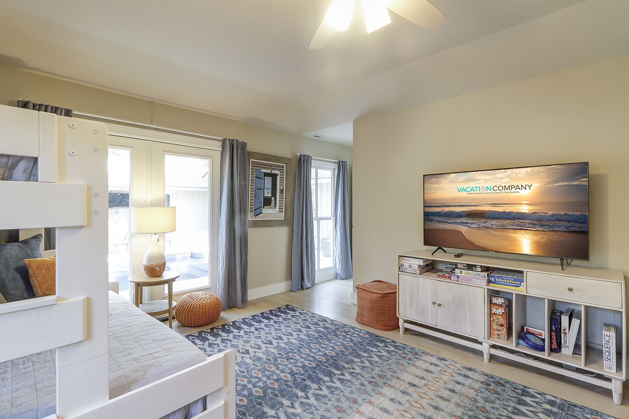 A modern hotel room with a bed, a TV, a bookshelf, and a view of the beach.