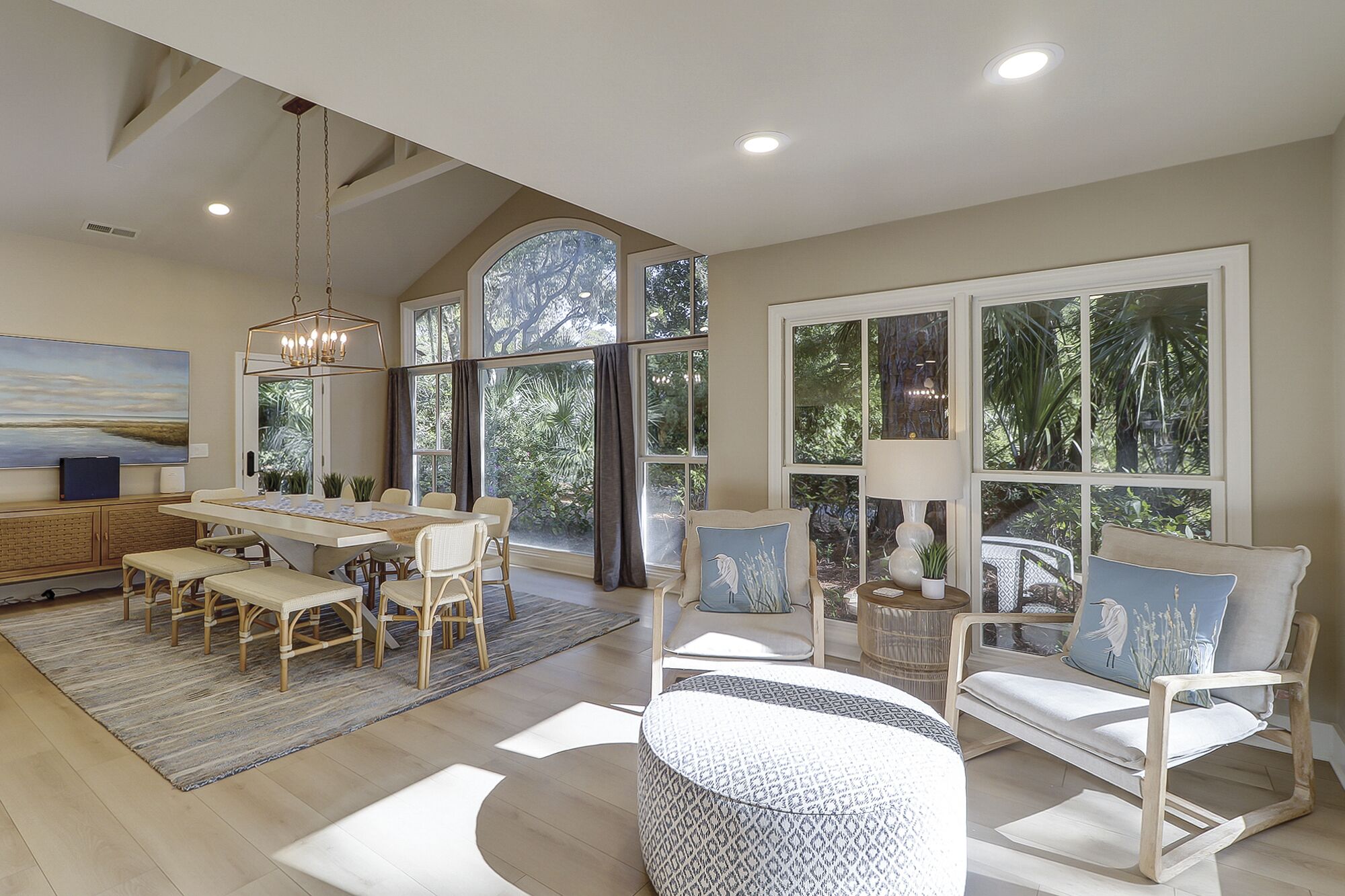 A spacious living area with a dining table, chairs, and a large window offering a view of greenery.