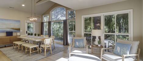 A spacious living area with a dining table, chairs, and a large window offering a view of greenery.