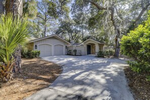 A two-car garage with a covered driveway, surrounded by mature trees and landscaping.