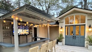 Un espace bar extérieur comprenant un comptoir, des tabourets de bar et un écran de télévision diffusant un événement sportif.