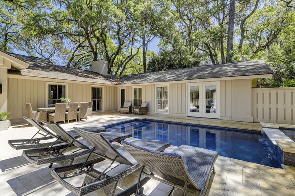 A backyard with a swimming pool, lounge chairs, and a dining area.