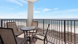 Un balcon avec une table et des chaises, donnant sur une plage sous un ciel dégagé.
