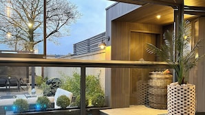 Area esterna moderna con vasca idromassaggio, struttura in vetro, terrazza in legno e vista sul giardino.