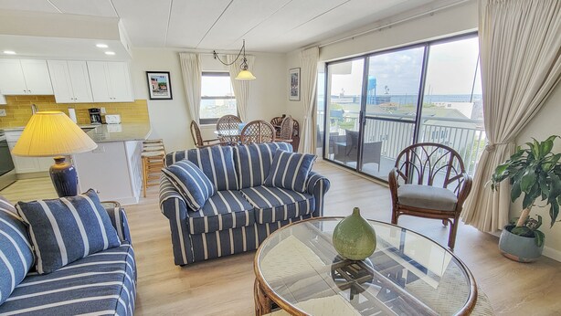 A spacious living area with a striped sofa, a round glass table, and a balcony with a view.