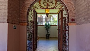 Un arcoado de entrada con detalles en metal, que da a un pasillo con baldosas, una planta en maceta y una lámpara colgante.
