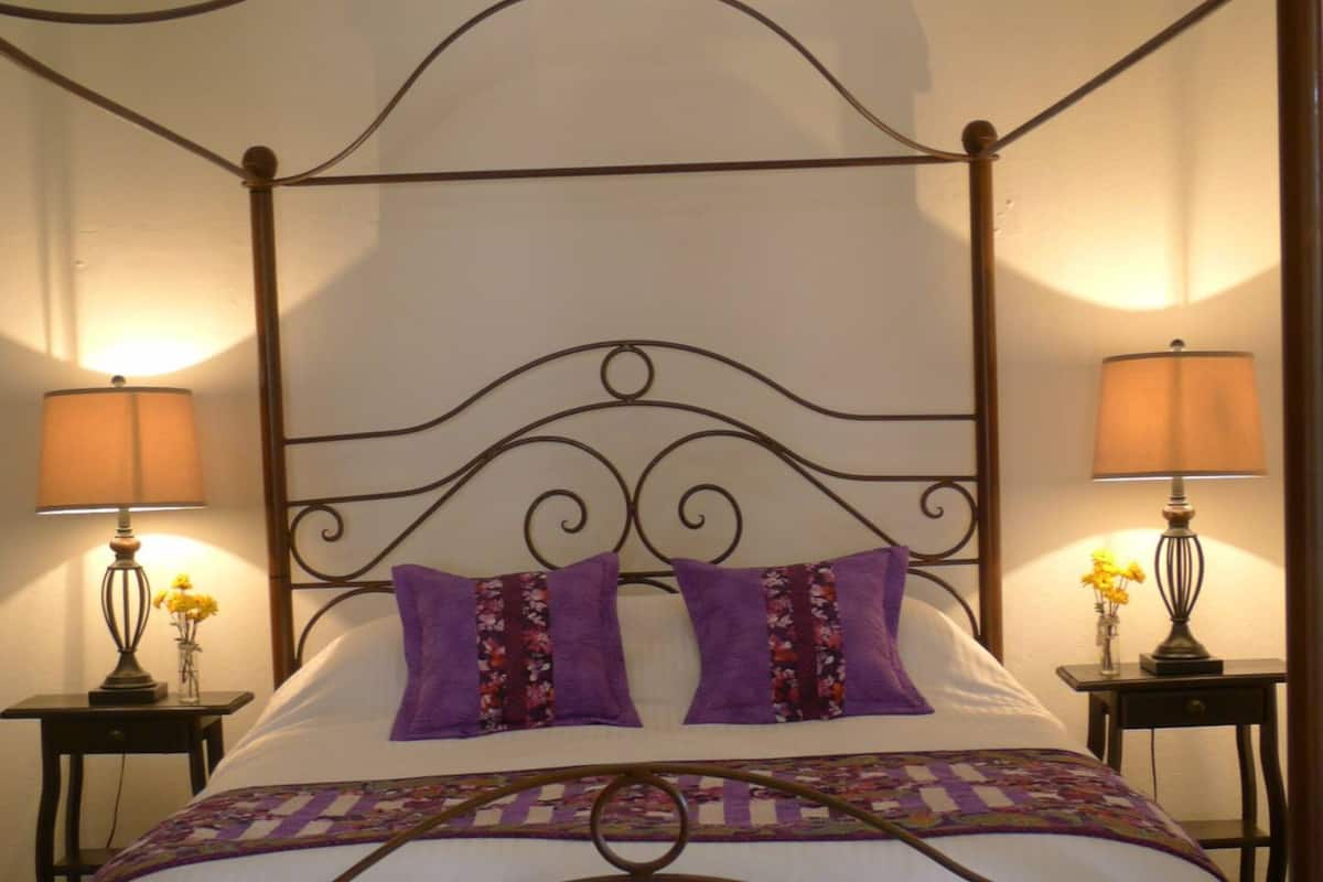 A four-poster bed with a metal frame, two bedside tables with lamps, and a floral-patterned bedspread.