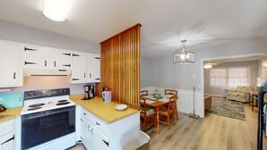 A compact kitchen with white cabinets, a stove, and a dining area with a wooden table and chairs. - Turtle's Nest Duplex 3 bedrooms, 2 bathrooms (Jekyll Island)