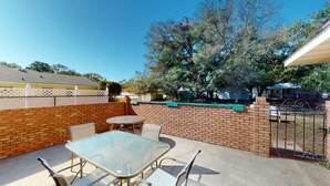 A patio with a glass table and chairs, a brick wall, and a tree in the background. - Turtle's Nest Duplex 3 bedrooms, 2 bathrooms (Jekyll Island)