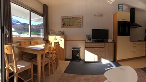 Une pièce confortable avec une table à manger, des chaises, un téléviseur, un coin cuisine et une vue sur les montagnes par la fenêtre.