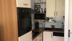 Une cuisine compacte équipée d’une cuisinière, d’un four, d’un four à micro-ondes et d’un évier. On y trouve des placards et un plan de travail sur lequel sont disposés divers objets.