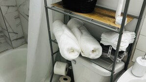 A bathroom with a toilet, a sink, a shower curtain, a metal shelf with towels and toiletries, and a trash bin. - Pet friendly fully furnished and private 1 Bedroom Flat (Fond du Lac)