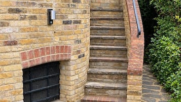 A stone staircase leading to a brick wall with a metal railing, a door, and a small window.