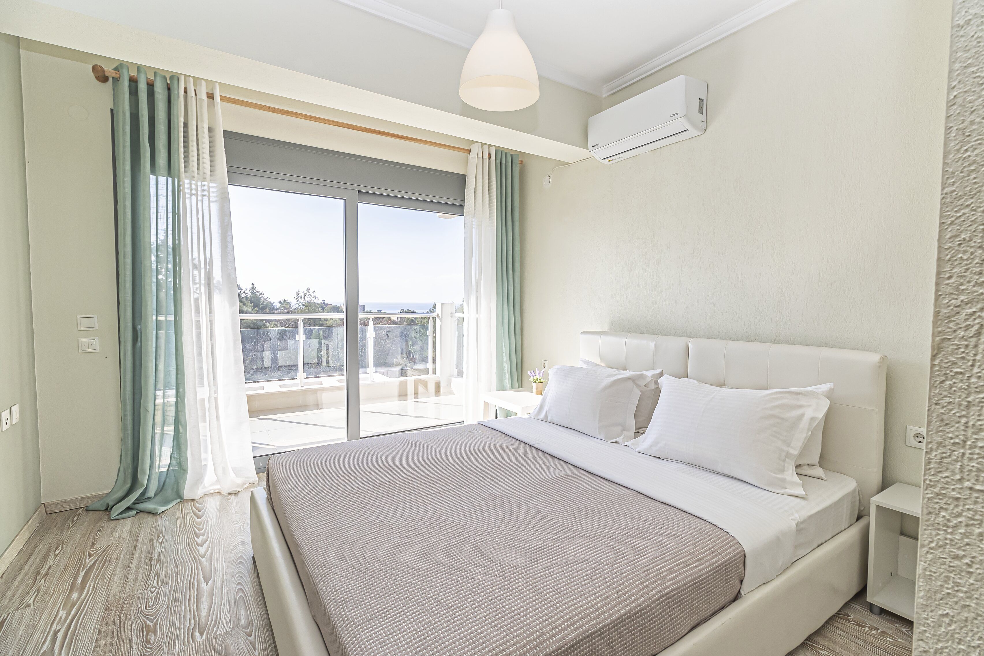 Ein Schlafzimmer mit einem großen Bett, einem Nachttisch, einer Deckenleuchte und Blick ins Freie.