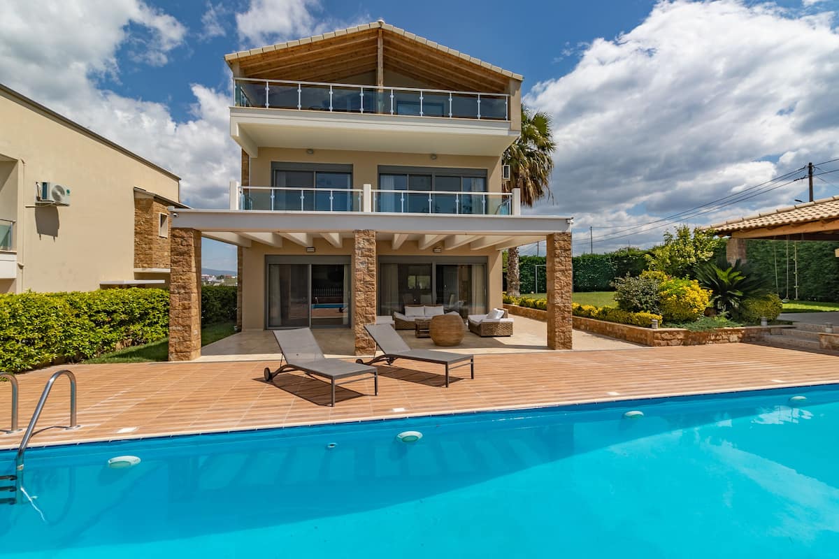 Une maison à deux étages avec une piscine, un espace salon extérieur et une terrasse couverte.