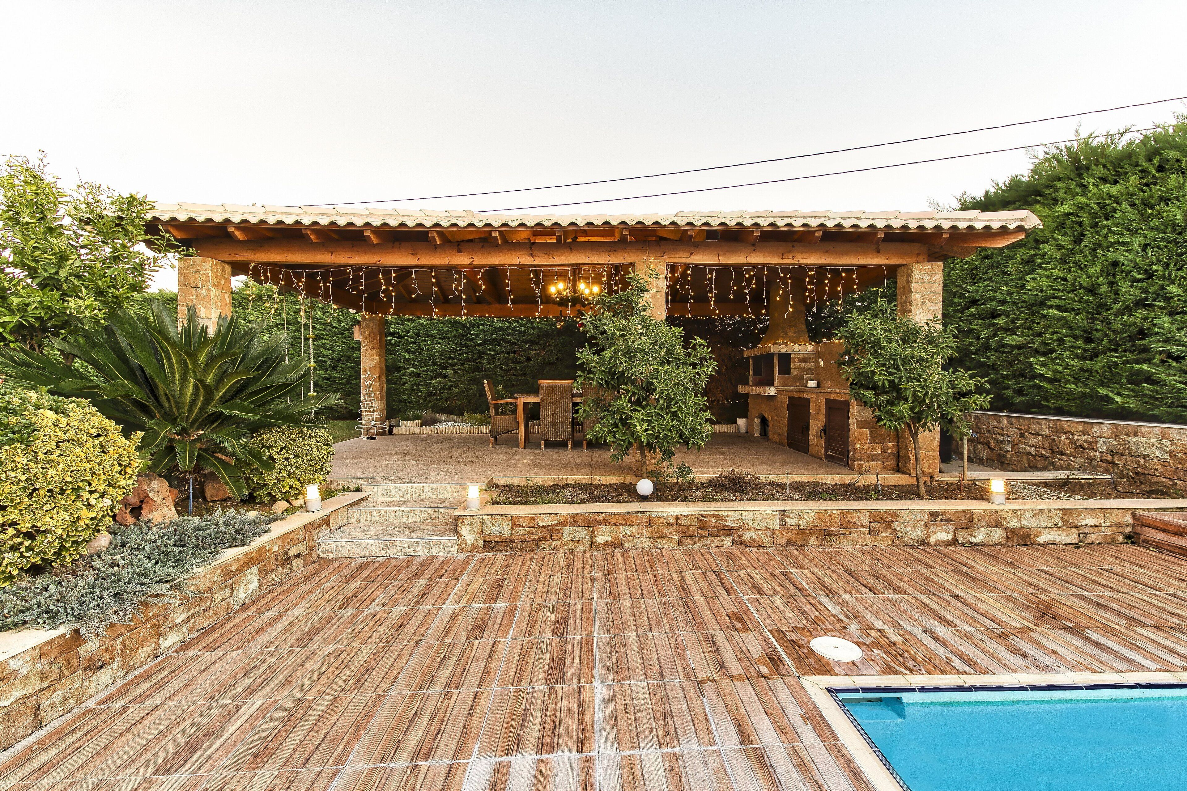 Une terrasse en bois avec une piscine, entourée de murs en pierre et de verdure.