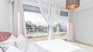 A bedroom with a large bed, white curtains, and a balcony with a glass railing. - Villa Nefeli (Nea Propontida)
